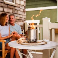 a man and woman sitting on chairs next to a table with a fire in it