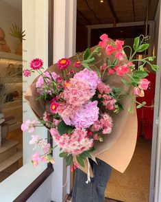 a person holding a bouquet of flowers in front of a store window with the door open