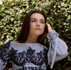 a woman in a blue and white top is posing for a photo with her hands on her head