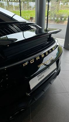 the back end of a black porsche car in a showroom with large windows and doors