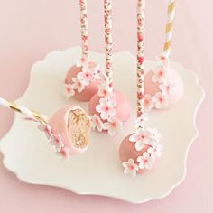 pink cake pops decorated with flowers on a white plate and gold straws in the middle