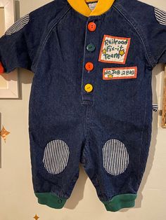 "Vintage 100% cotton denim railroad theme one piece children's romper. It has striped patches on the knees and sleeves. It has a button down closure, red sleeve hems, green pant hems, and a yellow collar. It has a \"railroad fix it team\" patch on the left chest as well as a \"no job 2 big\" patch. It has a large patch on the back that says \"working on the railroad\" Label: hopscotch  Size: 6-9 months  100% cotton  Measurements taken flat, please double where needed  Collar to sleeve hem: 9 inc Vintage Cotton Denim Jumpsuit With Button Closure, Vintage Cotton Overalls For Playtime, Cropped White Tee, Embroidered Denim Jacket, Ribbed Shirt, Tie Front Cardigan, Bubble Romper, Green Pants, Vintage Plaid