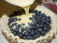 blueberries are being poured into a pie crust with cheese sauce on the top and bottom