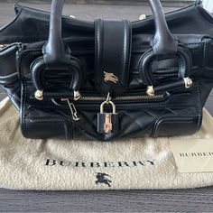 Authentic Burberry Purse Like-New Condition. Barely Ever Used. Black With Gold Hardware Features: Quilted Leather Body, Front Exterior Zip Pocket, Rolled Leather Handles, Front Strap With Padlock Closure, A Top Zip Closure, And An Interior Zip Pocket. Dimensions: Length: 14.5” Width: 6” Height: 8.5” Hand Drop: 12.00 Cm Shoulder Drop: 12.00 Cm Made In Italy Burberry Purse, Leather Handles, Quilted Leather, Burberry Bag, Leather Handle, Gold Hardware, Zip Pockets, Burberry, Satchel