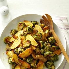 a white bowl filled with potatoes and brussel sprouts next to a wooden spoon