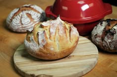 three loaves of bread sit on a cutting board next to a red dutch oven