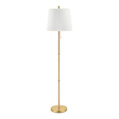 a gold floor lamp with a white shade on the base and a wooden stick in front of it