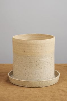 a white ceramic pot sitting on top of a wooden table next to a brown plate