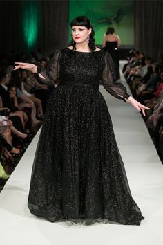 a woman in a black dress is walking down the runway