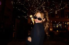 a woman with sunglasses on posing for a photo in front of some lights at night