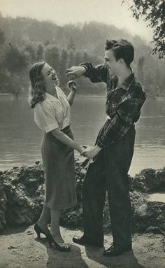 an old black and white photo of a man touching the hand of a woman in front of a lake