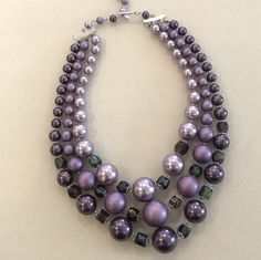 Fantastic pearl necklace with graduated round beads in various shades of purple. The shortest row is designed with lavender pearls, the middle row is designed with matte purple beads and the longest row is designed with a deeper purple pearlized color. There are faceted 12 amethyst crystals manipulated between the pearls in the front of the necklace. The beads are graduated in size and the colors are tonal that create a very fashionable look. Purple Pearl Necklaces With Round Beads, Purple Pearl Single Strand Necklace, Purple Single Strand Pearl Necklace, Adjustable Purple Pearl Necklace With Round Beads, Adjustable Beaded Purple Pearl Necklace, Adjustable Purple Pearl Necklace, Adjustable Purple Beaded Pearl Necklace, Purple Beaded Pearl Necklace, Elegant Lavender Beaded Necklace With Polished Beads