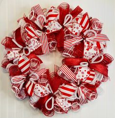 a red and white christmas wreath hanging on a door with ribbon around the wreath,