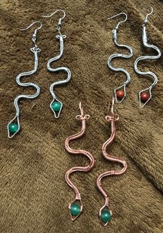 four pairs of earrings are laying on a towel next to each other, with one earring in the shape of a snake's tail