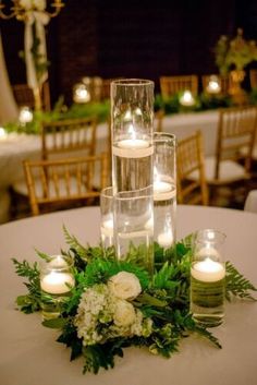 the centerpiece is surrounded by candles, greenery and white flowers in glass vases