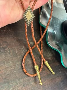 This awesome bolo tie has a metal diamond design. The cord is genuine brown leather. Our bolos pair nicely with many of our belt buckles! They make wonderful gifts.    The western bolo tie rope length is 39'' ; charm pendant size is 1 1/4'' tall Gold Bolo Tie, Bolo Ties For Men, Bolo Tie Aesthetic, Adjustable Gold Western Bolo Ties, Vintage Bolo Tie With Adjustable Length For Western Events, Vintage Bolo Ties With Adjustable Length For Western-themed Events, Vintage Adjustable Bolo Tie For Formal Occasions, Adjustable Formal Bolo Tie With Concho, Adjustable Western Bolo Tie For Formal Occasions