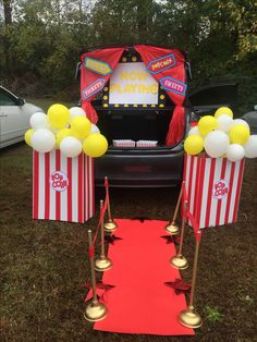 the back of a car with popcorn boxes and balloons on it, next to a red carpet