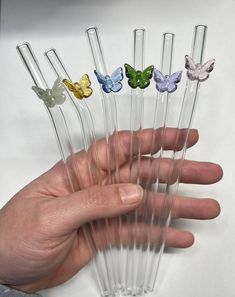 a hand is holding seven glass butterfly wands in different colors and sizes, each with one individual's finger