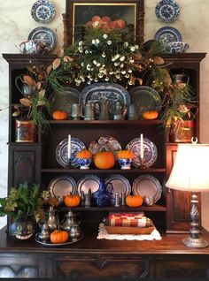 an old china cabinet with plates and flowers on the top, surrounded by other decorations