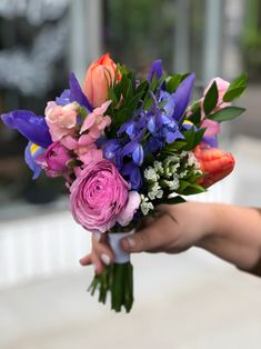 a bouquet of flowers being held by someone's hand in front of a building