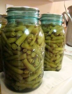 three jars filled with green beans sitting on top of a counter