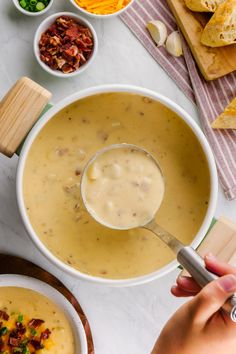 a person is spooning soup into a bowl with other bowls and bread on the side