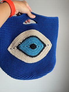 a crocheted blue bag with an eye on the front and bottom, held by a woman's hand