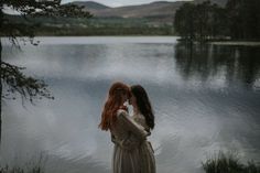 two women standing next to each other in front of a lake