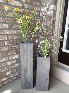 two wooden vases with flowers in them sitting next to a brick wall and window