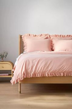 a bed with pink sheets and pillows on top of it in a room next to a dresser