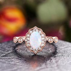 a white opal and diamond ring sitting on top of a piece of wood with flowers in the background