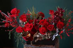 a bouquet of red roses and other flowers in a wooden box with greenery on top