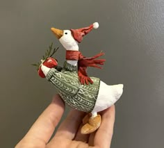 a hand holding a small figurine of a duck wearing a scarf and hat