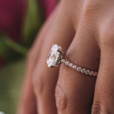 a woman's hand with a diamond ring on top of her finger and a flower in the background