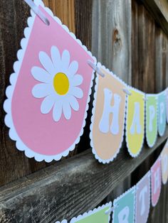 a happy birthday banner hanging from a wooden fence with daisies on the bunting