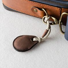 a brown and blue bag with a leather tag attached to the strap that is hanging from it's side