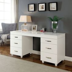 a white desk with three drawers in front of a window and pictures on the wall