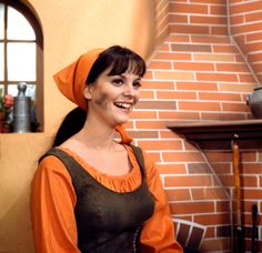 a woman in an orange and black dress standing next to a brick wall smiling at the camera