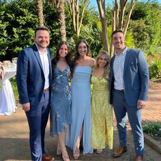 three men and two women posing for a photo in front of some trees at a wedding