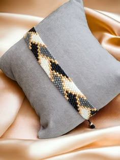 a gray pillow with a beaded bracelet on it