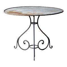 an iron table with white marble top and scrolled design on the base, against a white background