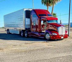 a red semi truck parked in a parking lot with palm trees and blue sky behind it