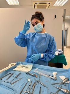 a woman in scrubs and surgical gloves standing next to a table filled with medical equipment