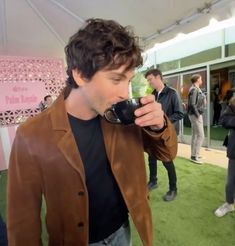 a man drinking from a coffee cup while standing on top of a green grass covered field