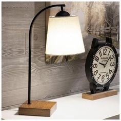 a clock sitting on top of a white table next to a lamp and wooden block