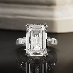 an emerald - cut diamond ring with baguets sits on a reflective surface