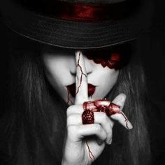 a woman with blood painted on her face holding a finger up to her mouth while wearing a black hat