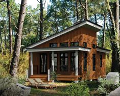 a small house in the woods with deck chairs on the grass and trees around it