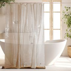 a white bath tub sitting under a window next to a plant in a potted planter