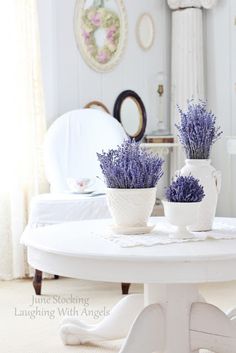 two white vases with lavender flowers sitting on a table